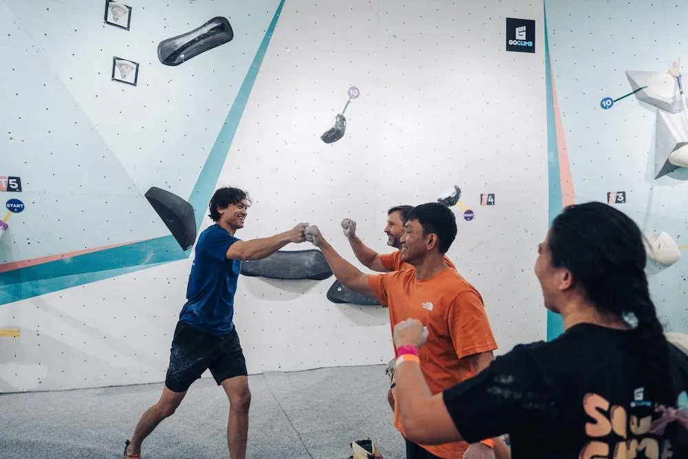 A climbing team topping out a boulder route and exchanging fistbumps
